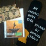 Die CD von "Hamilton", neben zwei 10-Dollar-Scheinen und Socken mit der Aufschrift "My thoughts have been replaced by Hamilton Lyrics"