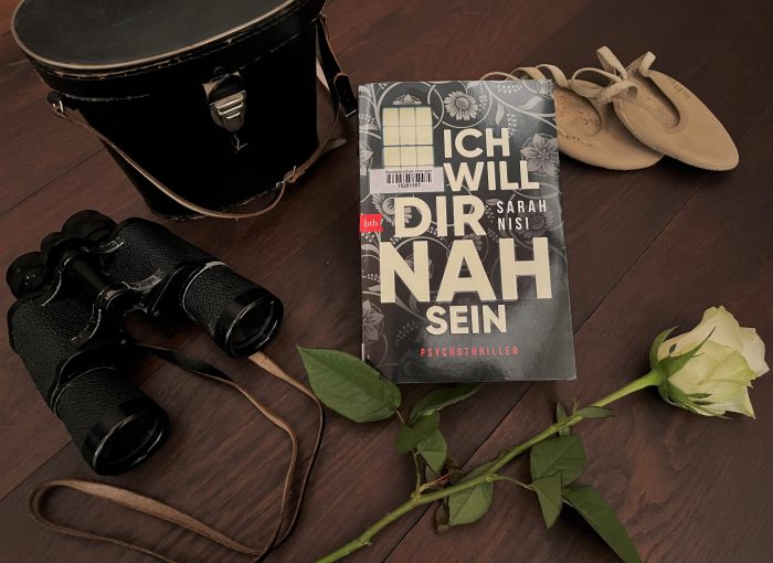 Das Buch Ich will dir nah sein von Sarah Nisi liegt zwischen einem Fernglas, einer weißen Rose und Tanzschuhen.