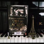 Buch Stadt der Mörder von Britta Habekost auf Klaviertasten neben Eiffelturm-Modell
