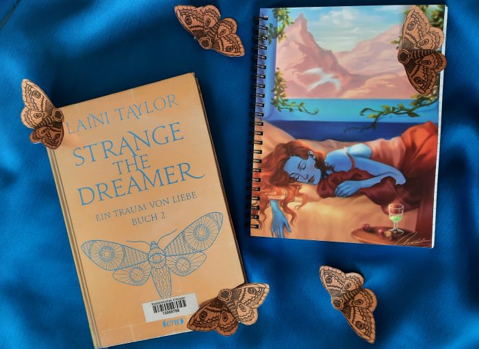 Das Buch "Strange the Dreamer" liegt auf einem blauen Hintergrund neben einer Illustration.