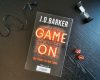 Buch "Game on" von J. D. Barker auf Tisch mit Mikro, Sanduhr und Würfeln arrangiert